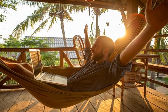 Mann mit Laptop liegt in der Hängematte