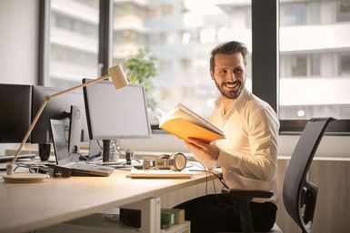 Mann lachend am Schreibtisch im Büro