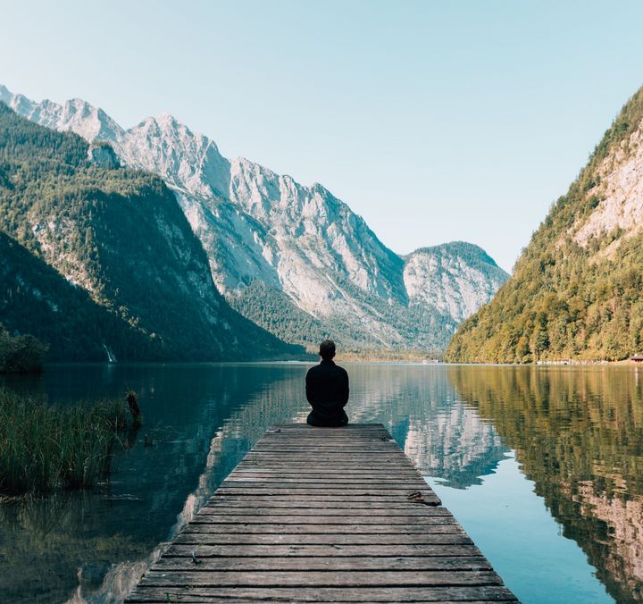 Mann sitzt auf dem Steg am See mit Bergen