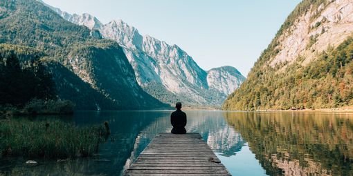 Mann sitzt auf dem Steg am See mit Bergen