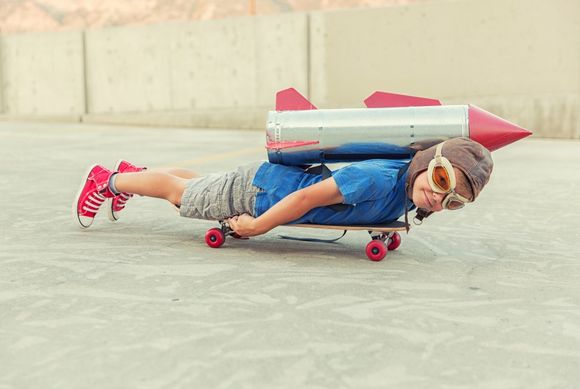 Junge mit Rakete auf dem Ruecken auf Skateboard liegend