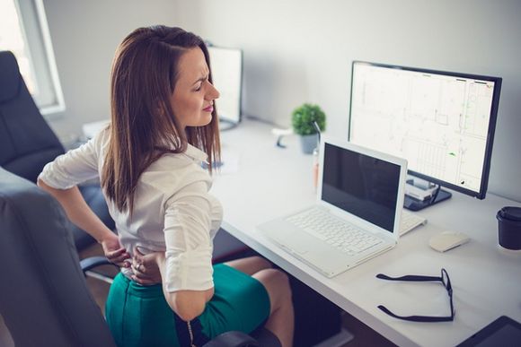 Frau mit Rückenschmerzen vor dem Laptop